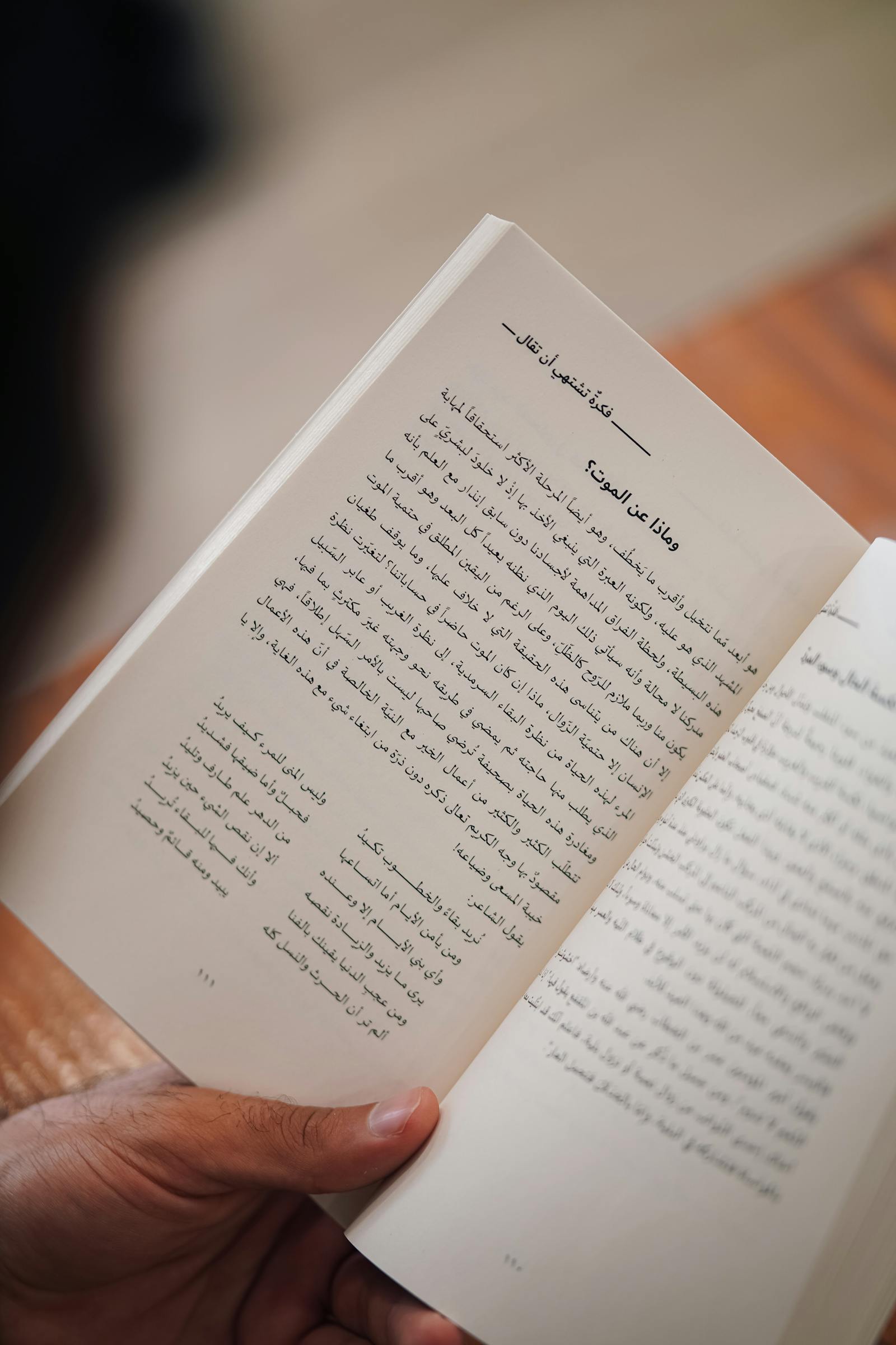 A reader holding an open contemporary Arabic-language book — Pearson Edexcel International GCSE Arabic (First Language) study resources